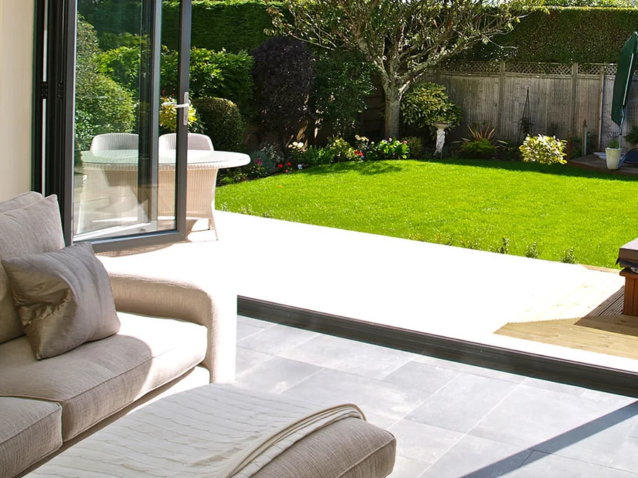 Bifold doors open onto a patio and lawn, seen from a sofa inside