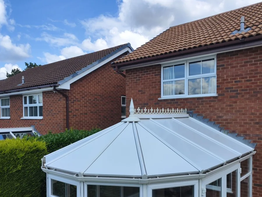 White Victorian-style conservatory with a glazed roof beside a red-brick house