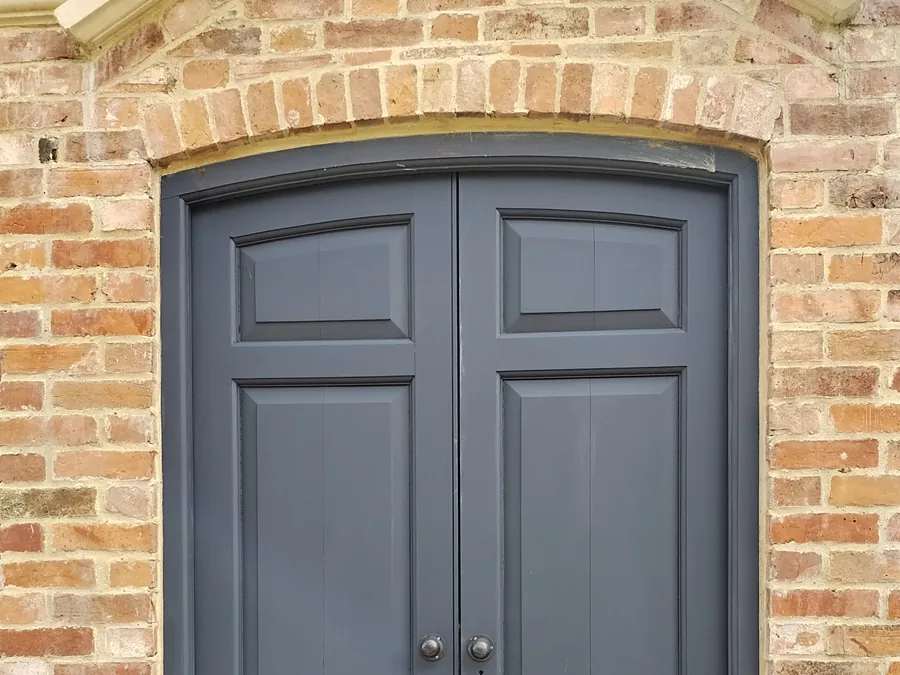 Grey panelled double front doors under a brick arch